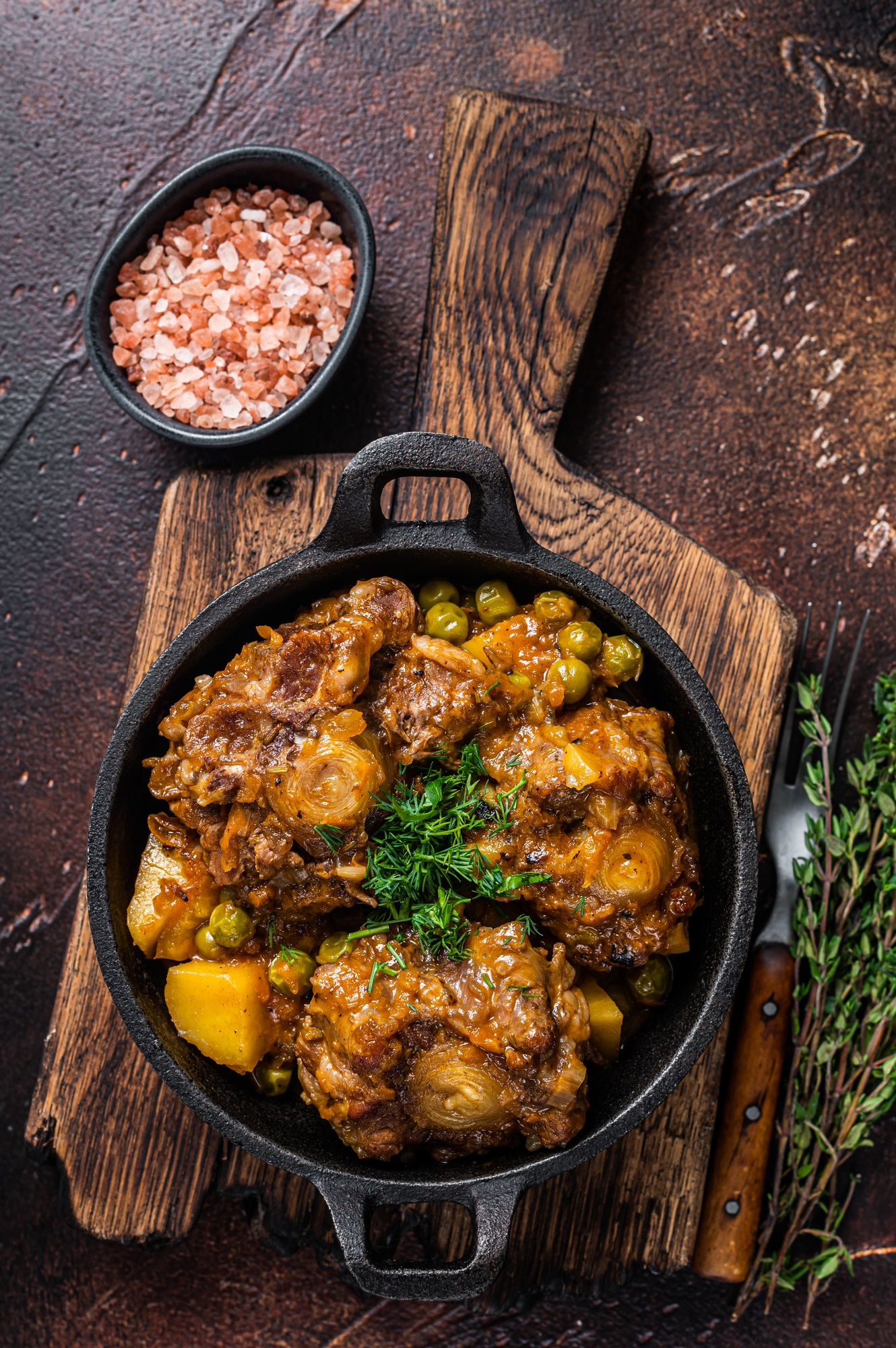 Beef oxtails stew with wine and vegetables in a pan. Dark background. Top view